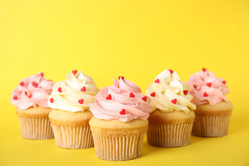 Tasty cupcakes with heart shaped sprinkles on yellow background. Valentine's Day celebration