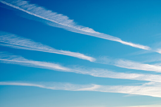 Background with blue sky and parallel airplane exhaust tracks. White chemtrails