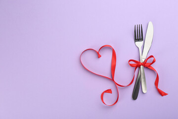 Beautiful cutlery set and red ribbon on violet background, flat lay with space for text. Valentine's Day dinner