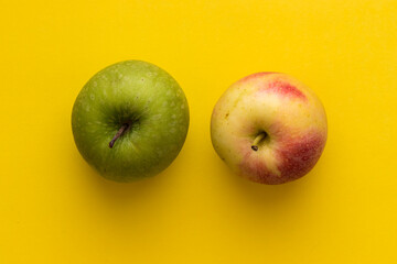 Green apple and yellow-red apple on a yellow background