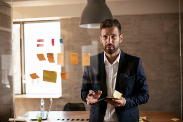 Fototapeta premium Businessman in conference room use sticky notes on glass wall. Handsome businessman making a business plan..