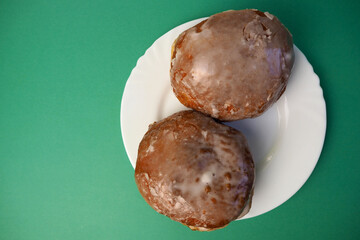 two donuts in sugar glaze lie in a white round plate view on a green background top view