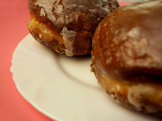 close up two donuts in sugar glaze lie in a white round plate on a pink background side view