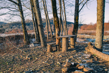 An old wooden bench in the forest in a clearing covered with melting snow on a sunny day.