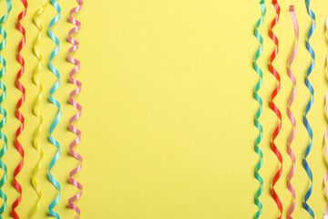 Colorful serpentine streamers on yellow background, flat lay. Space for text