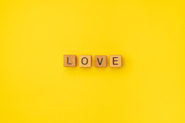 Wooden cubes with the word Love on a colorful yellow background. Word of love are made of letters from wood for your girlfriend, boyfriend, for Valentines Day greeting romantic postcard