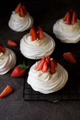 Anna Pavlova cake with cream and fresh strawberries on a dark background,