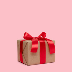 Gift box tied with red ribbon on a pink background with copy space. Minimal composition with copy space.