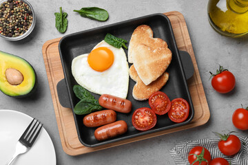 Romantic breakfast with fried sausages, heart shaped egg and toasts on grey table, flat lay. Valentine's day celebration