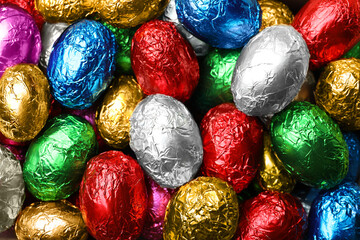 Fototapeta na wymiar Chocolate eggs wrapped in colorful foil as background, top view