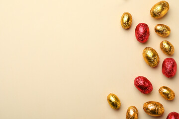 Chocolate eggs wrapped in red and golden foil on beige background, flat lay. Space for text