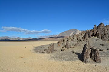 The Grandstand on the Racetrack Playa in the Death Valley National Park, a very dark grey rock surrounded by featureless, light tan-colored clay sediment in a dry lake bed