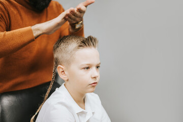 the process of hair styling a blond boy with with hair dryer and comb in a chair in a barbershop salon, a barbershop concept for men and boys