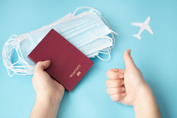 Person holding a passport on a blue background wearing surgical masks and pointing thumb up