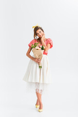 smiling pin up woman looking at camera while holding flowers on white
