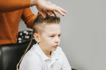Fototapeta premium the process of hair styling a blond boy with with hair dryer and comb in a chair in a barbershop salon, a barbershop concept for men and boys