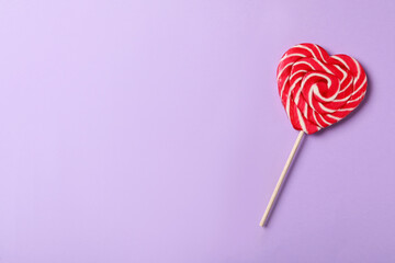 Sweet heart shaped lollipop on violet background, top view with space for text. Valentine's day celebration