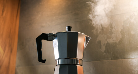 An Italian espresso mokka machine with steam getting out of it while making a fresh coffee in a regular kitchen with wood and stone background
