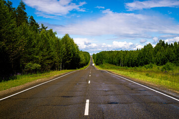 An asphalt road outside the city, after the last rain. Intercity deserted track passing through a summer forest.