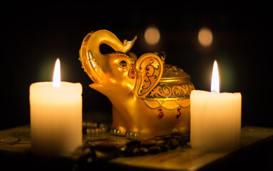 Close-up still life with a figurine of an Indian golden elephant and burning candles