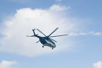High in the sky with beautiful clouds, a passenger helicopter is flying, painted in blue and gray. Close-up