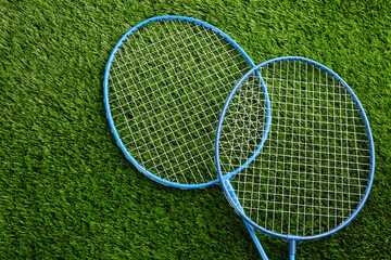 Badminton rackets on green grass outdoors, above view. Space for text