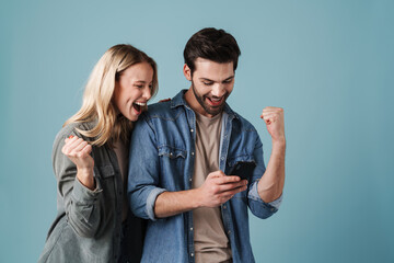 Young delighted man and woman making winner gesture while using cellphone