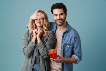 Young happy man with gift box covering eyes of excited girl