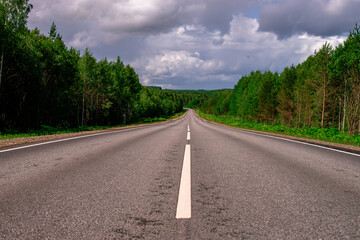 An asphalted intercity road with white markings extending into the distance through a green forest.