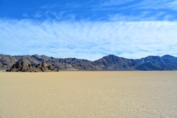 The Grandstand on the Racetrack Playa in the Death Valley National Park, a very dark grey rock surrounded by featureless, light tan-colored clay sediment in a dry lake bed