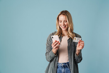 Cheerful beautiful blonde girl posing with credit card and mobile phone