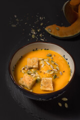 Pumpkin cream soup with seeds and croutons on a black background