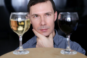 Choosing alcohol, man looks at the glasses with white and red wine. Sommelier, tasting and party concept