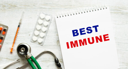 BEST IMMUNE is written in a notebook on a white table next to pills and a stethoscope.