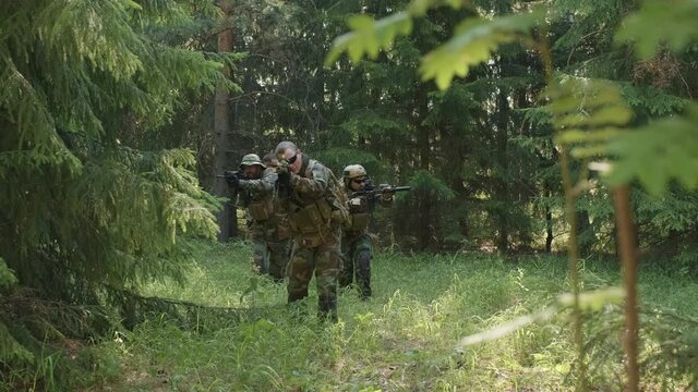 Tracking medium closeup of squad of professional military surveillance officers walking through summer forest towards camera, looking through rifle day scope for enemies