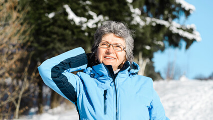 Portrait of smiling elderly woman with glasses outdoors. Pensioner walking on a sunny winter day.