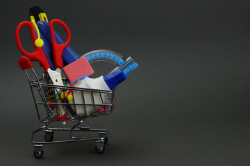 Shopping cart with stationery, school supplies on gray background