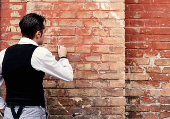 Back view of view of retro-styled man drawing with chalk on a brick wall.