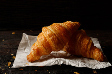 freshly baked croissants set of delicious fresh in wax paper plates on wooden dark table. French breakfast. top view Copy space.