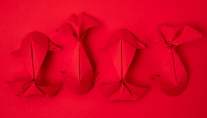 Four red paper origami koi carp fishes on a matching red background alternating directions in a row