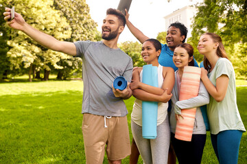 fitness, sport and healthy lifestyle concept - group of happy people with yoga mats taking selfie with smartphone at park