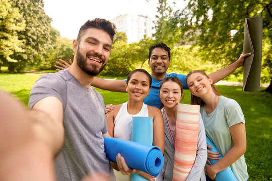 fitness, sport and healthy lifestyle concept - group of happy people with yoga mats taking selfie at park