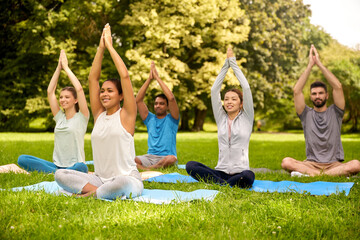 fitness, sport, yoga and healthy lifestyle concept - group of people meditating in lotus pose at summer park