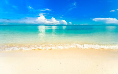 Beautiful background image of tropical beach. Light surf wave with white foam. Blue summer sky, white clouds reflected in turquoise clear water ocean. Relaxation and rest.
