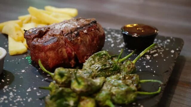 plato de carne cocinada en su punto, con patatas fritas, pimientos y salsas, plano detalle girando