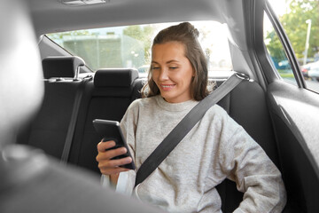 transport, vehicle and technology concept - happy smiling woman or female passenger in taxi car using smartphone