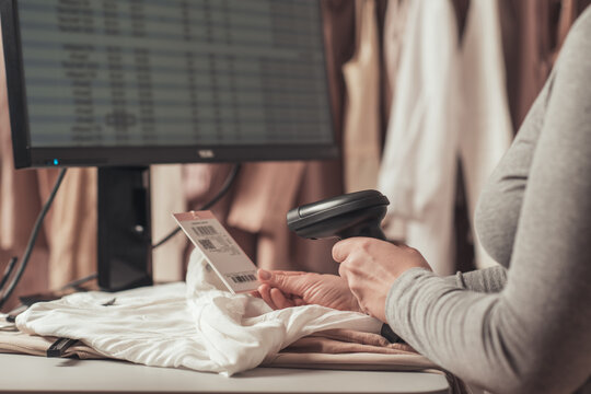 Woman Cashier, Seller Scanning And Reading  Barcode From Clothes Using Barcode Scanner In Female Clothing Store.