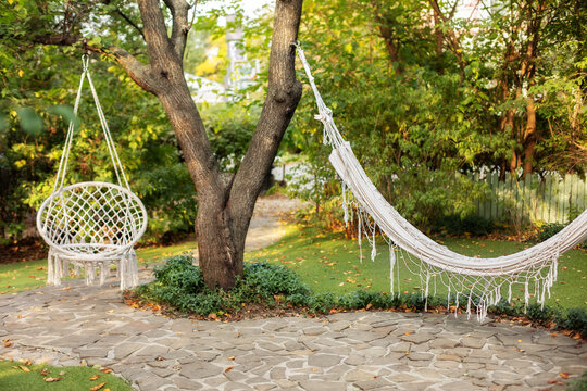 Comfortable Hanging Wicker White Chair In Summer Garden. Cozy Hygge Place For Weekend Relax In Garden. Hammock Chair In Boho Style Hanging On Tree. Cozy Exterior Backyard. Concept Of Rest Outdoor. 
