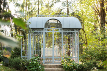 Wrought metal gazebo in summer garden. Flowers in pots near porch. Sofa in spring gazebo. Large iron blue gazebo for relax outdoor. Wedding decorations. exterior Romantic alcove. Decor autumn terrace 