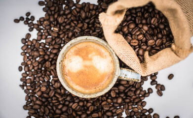Espresso shot in a clay mug placed on top of roasted coffee beans spilled on the ground.